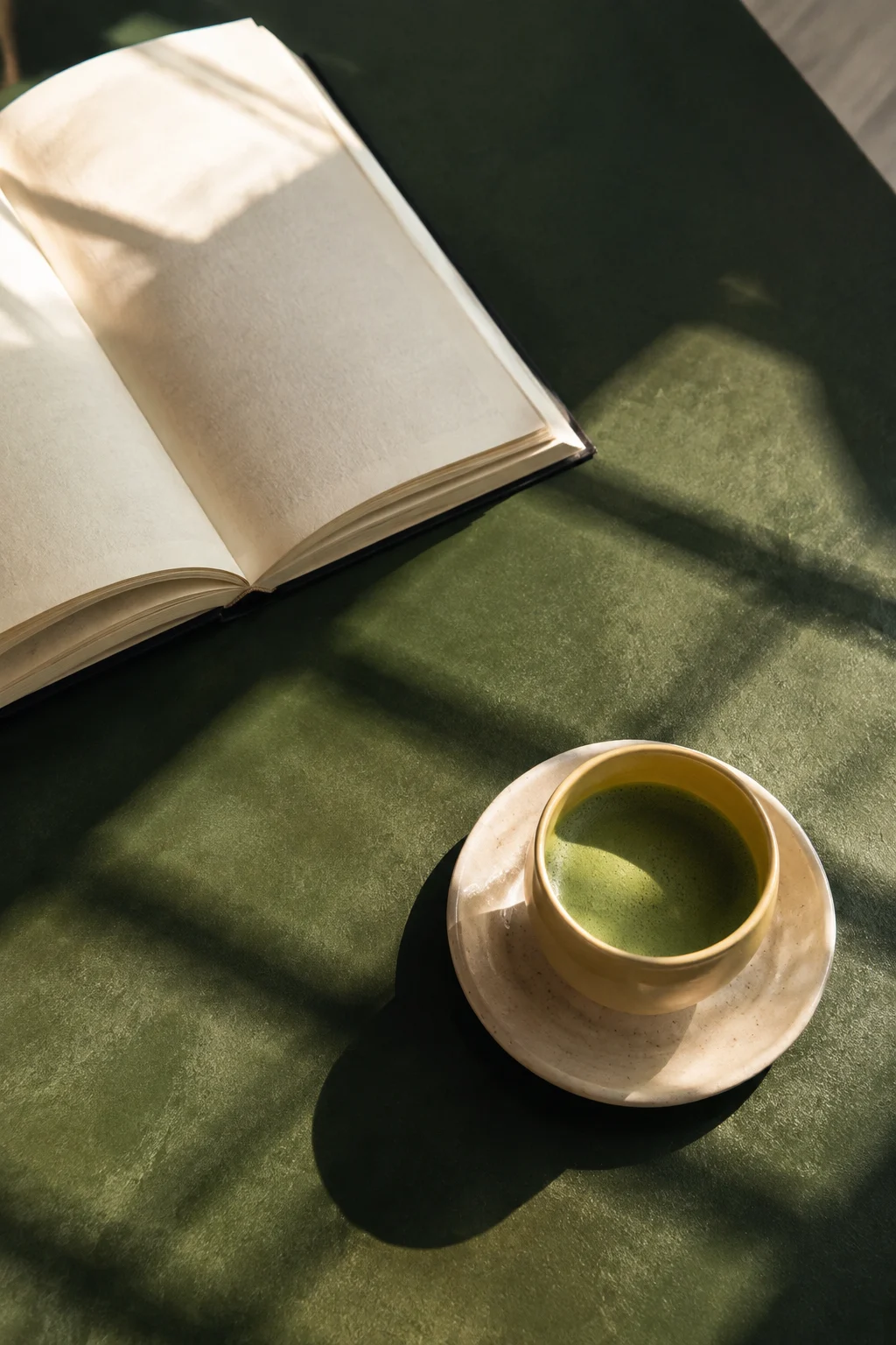 Morning sunlight across a green table, a ceramic cup of matcha and an open book